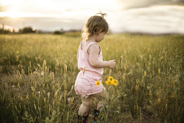 Mädchen spaziert inmitten eines grasbewachsenen Feldes gegen den Himmel - CAVF37699