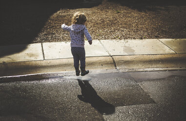 Rückansicht eines spielenden Mädchens auf nasser Straße an einem sonnigen Tag - CAVF37705