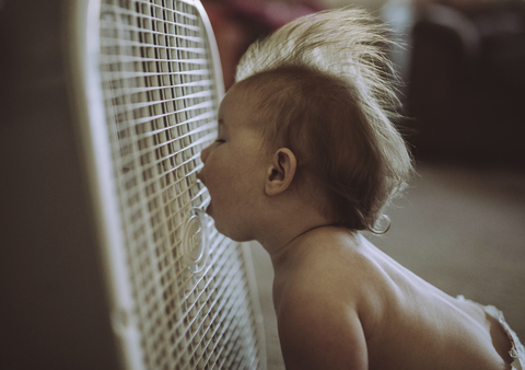 Hemdloser kleiner Junge mit offenem Mund genießt die Brise der Klimaanlage zu Hause, lizenzfreies Stockfoto