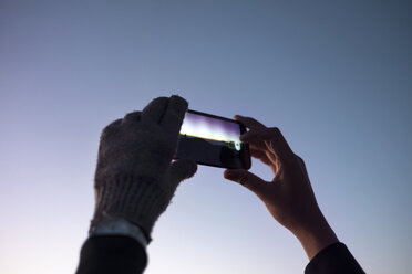 Ausgeschnittenes Bild von Händen, die mit einem Smartphone gegen den klaren Himmel in der Abenddämmerung fotografieren - CAVF37716