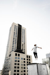 Low angle view of man jumping on building terrace against clear sky - CAVF37724