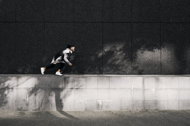 Side view of man running on retaining wall on sunny day - CAVF37729