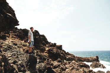 Seitenansicht eines jungen Mannes, der auf einem Felsen am Meer steht, gegen den Himmel - CAVF37755