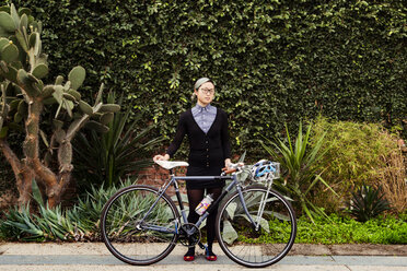 Porträt einer Geschäftsfrau mit Fahrrad vor Pflanzen stehend - CAVF37765