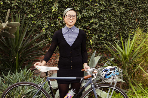 Portrait of happy businesswoman standing with bicycle against plants - CAVF37766