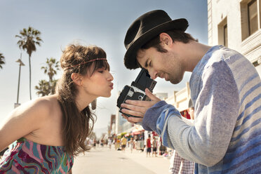 Side view of woman puckering lips while man photographing through vintage camera on sidewalk - CAVF37770