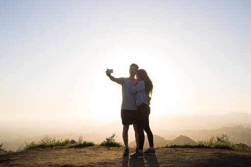 Paar, das ein Selfie mit dem Smartphone macht, während es auf einem Berg gegen den klaren Himmel steht - CAVF37809