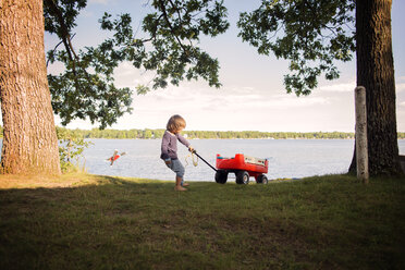 Junge spielt am See mit rotem Wagen - CAVF37860