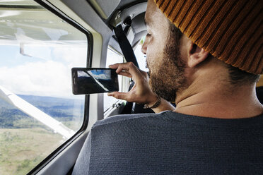 Rückansicht eines Mannes, der vom Flugzeugfenster aus mit seinem Smartphone die Landschaft fotografiert - CAVF37969