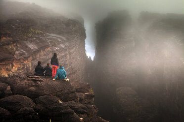 Rückansicht von Freunden, die bei nebligem Wetter auf einem Felsen sitzen - CAVF37988