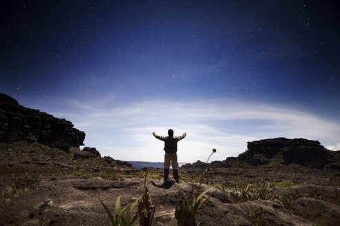 Rückansicht eines Mannes, der mit ausgestreckten Armen auf einem Berg gegen den Himmel in der Abenddämmerung steht - CAVF38002