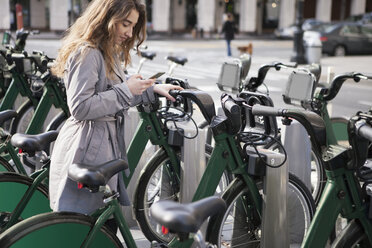 Junge Frau, die eine SMS über ihr Smartphone auf einem Fahrradparkplatz schreibt - CAVF38005