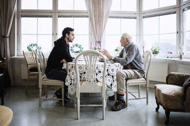 Side view of man communicating with caretaker at dining table - MASF03259