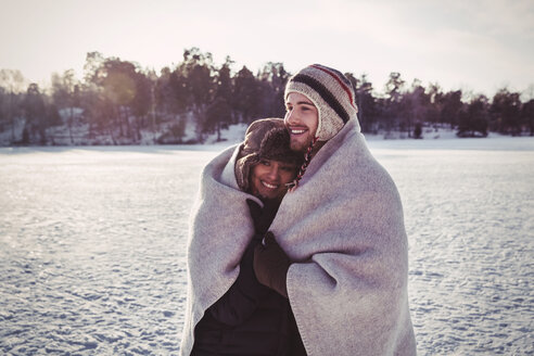 Smiling couple wrapped in blanket while standing on field during winter - MASF03263