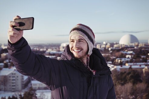 Smiling young man clicking selfie through smart phone during winter - MASF03264