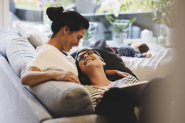 Smiling lesbian couple embracing while baby girl sleeping in living room at home - MASF03285