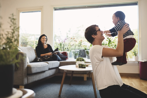 Lächelnde Frau sieht Mutter an, die mit Tochter im Wohnzimmer spielt, lizenzfreies Stockfoto