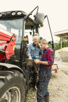 Frau diskutiert mit einem männlichen Arbeiter über ein Dokument, das von einem Traktor auf einem Bauernhof stammt - MASF03291