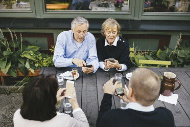 Two senior couples using mobile phones at table of outdoor restaurant - MASF03310