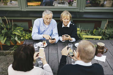 Zwei ältere Paare benutzen Handys am Tisch eines Restaurants im Freien - MASF03310