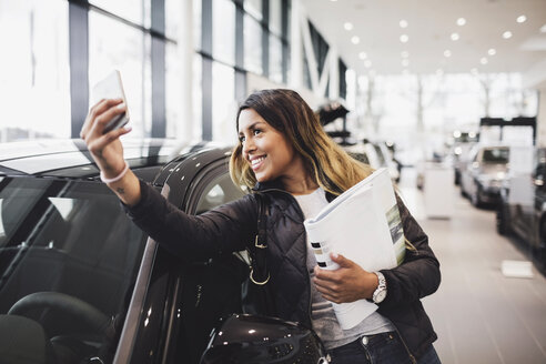 Lächelnde Frau macht Selfie mit neuem Auto im Ausstellungsraum - MASF03312