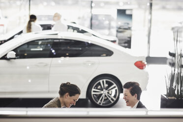 Smiling women discussing by car at showroom - MASF03313
