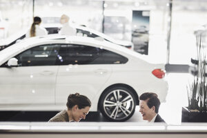 Lächelnde Frauen, die im Ausstellungsraum über ein Auto diskutieren - MASF03313