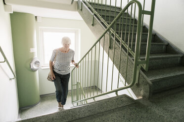 Ältere Frau geht auf einer Treppe in einem Mehrfamilienhaus - MASF03322