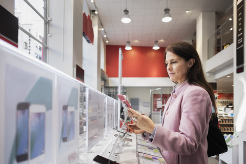 Seitenansicht einer Frau, die in einem Geschäft ein Smartphone benutzt, lizenzfreies Stockfoto