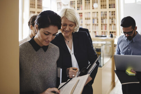 Lächelnde Juristinnen diskutieren beim Spaziergang mit Kollegen in der Bibliothek - MASF03333