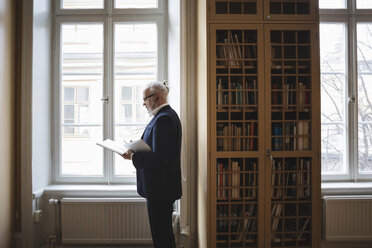 Ein älterer Fachmann liest ein Buch, während er über Kopfhörer in der juristischen Bibliothek zuhört - MASF03337