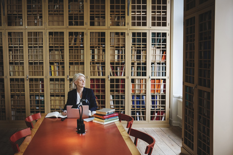 Älterer Berufstätiger schaut weg, während er an einem Tisch in einer juristischen Bibliothek sitzt, lizenzfreies Stockfoto