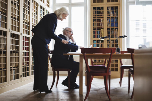 Seitenansicht eines älteren Anwalts und einer Anwältin, die am Tisch in einer Bibliothek diskutieren - MASF03340