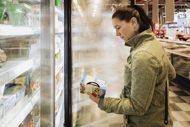 Seitenansicht einer Frau, die ein Lebensmitteletikett im Kühlregal liest - MASF03344