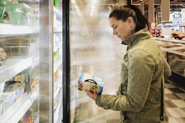 Side view of woman reading food label at refrigerated section - MASF03344