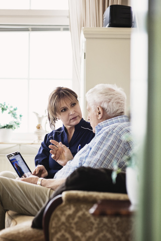 Senior man talking to caretaker while using digital tablet at nursing home stock photo