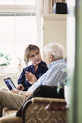 Senior man talking to caretaker while using digital tablet at nursing home - MASF03350