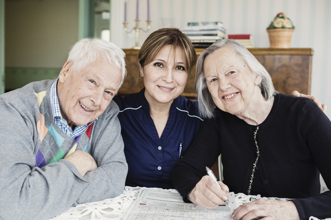 Porträt eines lächelnden Hausmeisters und älterer Menschen, die ein Kreuzworträtsel im Pflegeheim lösen, lizenzfreies Stockfoto