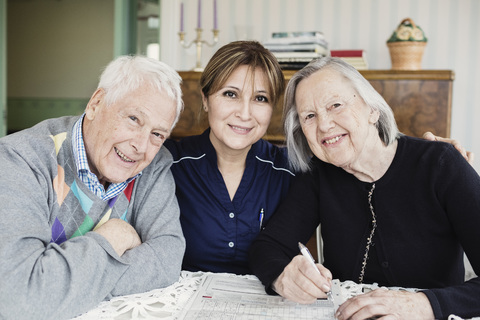 Portrait of smiling caretaker and senior people solving crossword puzzle at nursing home stock photo