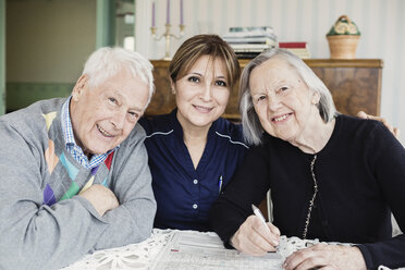 Portrait of smiling caretaker and senior people solving crossword puzzle at nursing home - MASF03352