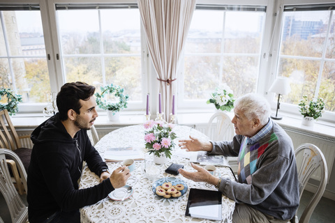 Senior man talking to caretaker at dining table in nursing home stock photo