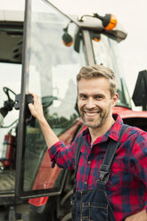Porträt eines lächelnden Mannes an einem Traktor auf einem Bauernhof - MASF03380