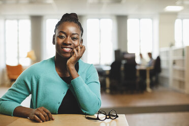 Portrait of smiling woman with hand on chin sitting by table - MASF03388