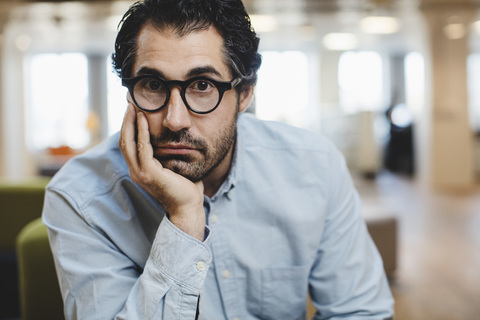 Portrait of man with hand on chin sitting at corridor stock photo