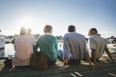 Rear view of two senior couples sitting on pier against clear sky - MASF03403