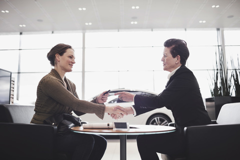 Saleswoman and customer shaking hands while talking at desk in showroom stock photo