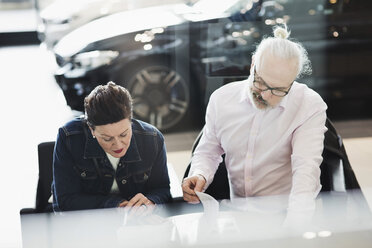 Senior man and woman reading documents while sitting at car showroom - MASF03409