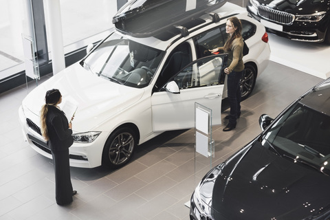 Saleswoman looking at customer examining car in showroom stock photo