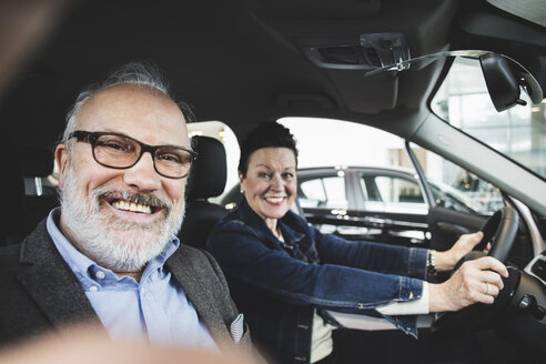 Portrait of happy senior man and woman sitting in car at showroom - MASF03413