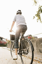 Rear view of woman cycling on road against clear sky - MASF03418